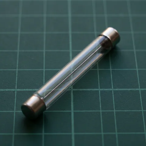Macro photo of a clear glass Geiger-Muller tube with metal end caps lying on dark green graph paper